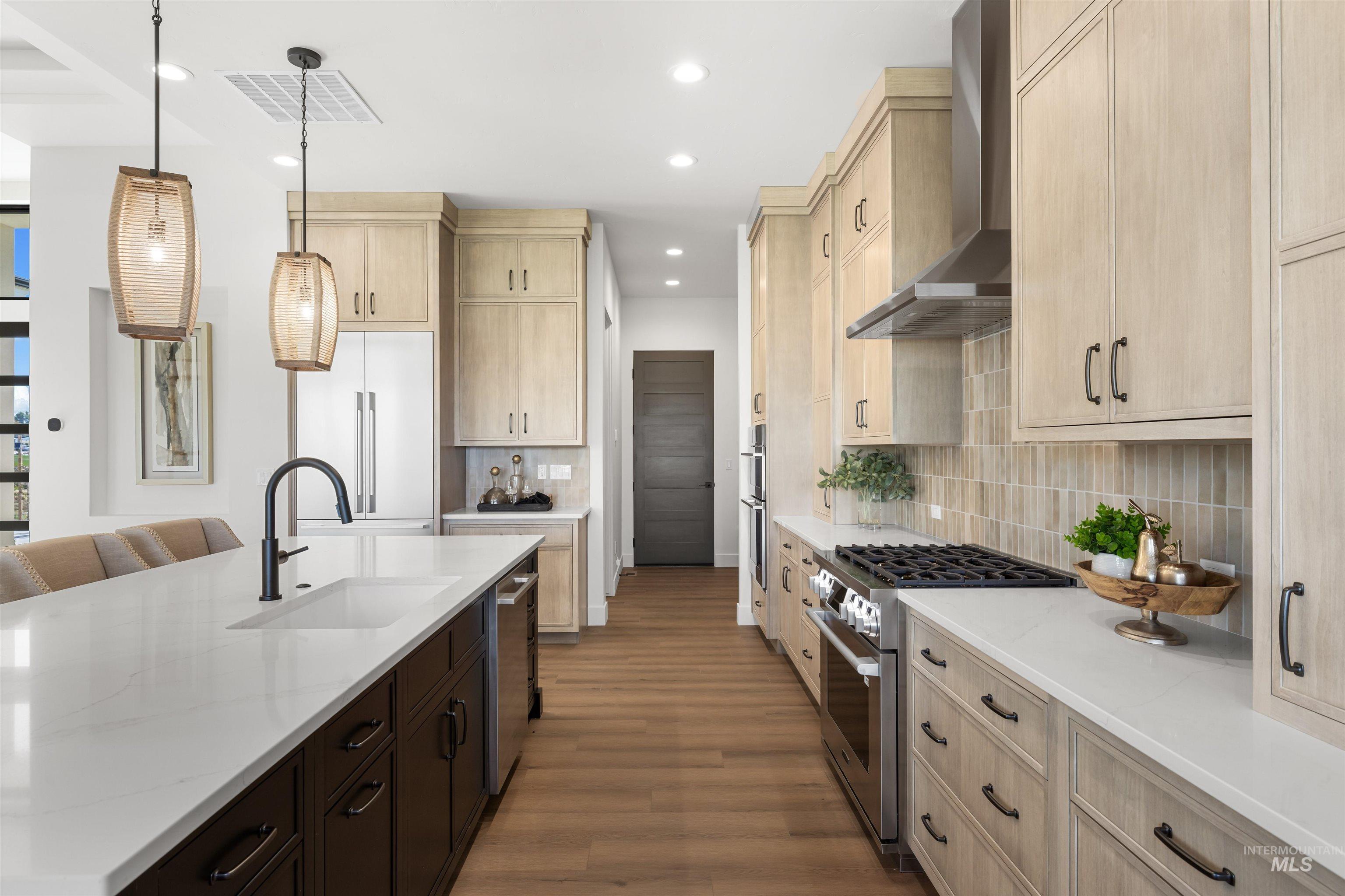 Kitchen with hanging light fixtures, stainless steel appliances, light stone counters, light brown cabinets, and recessed lighting