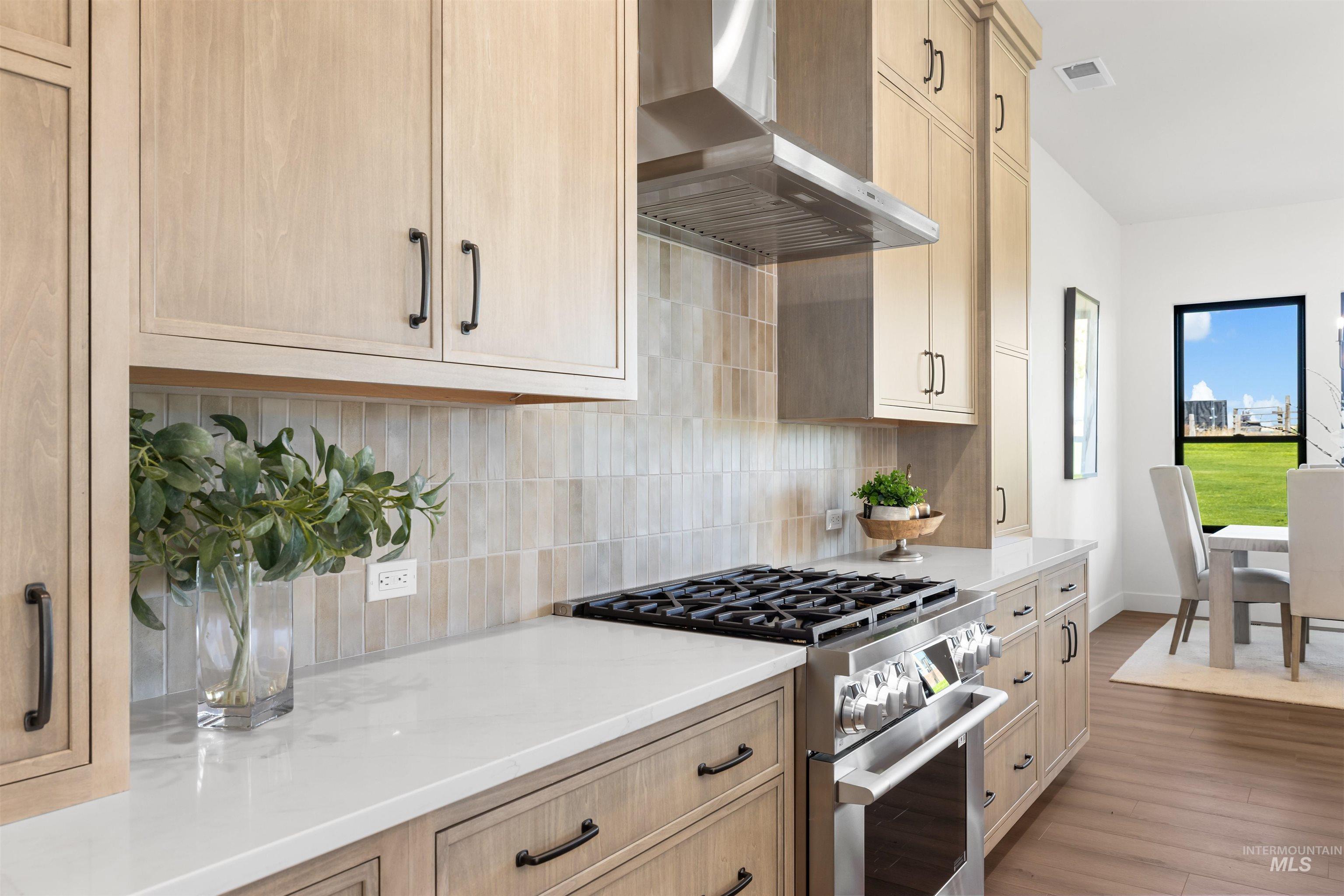 Kitchen featuring gas range, wall chimney range hood, tasteful backsplash, light stone countertops, and wood finished floors