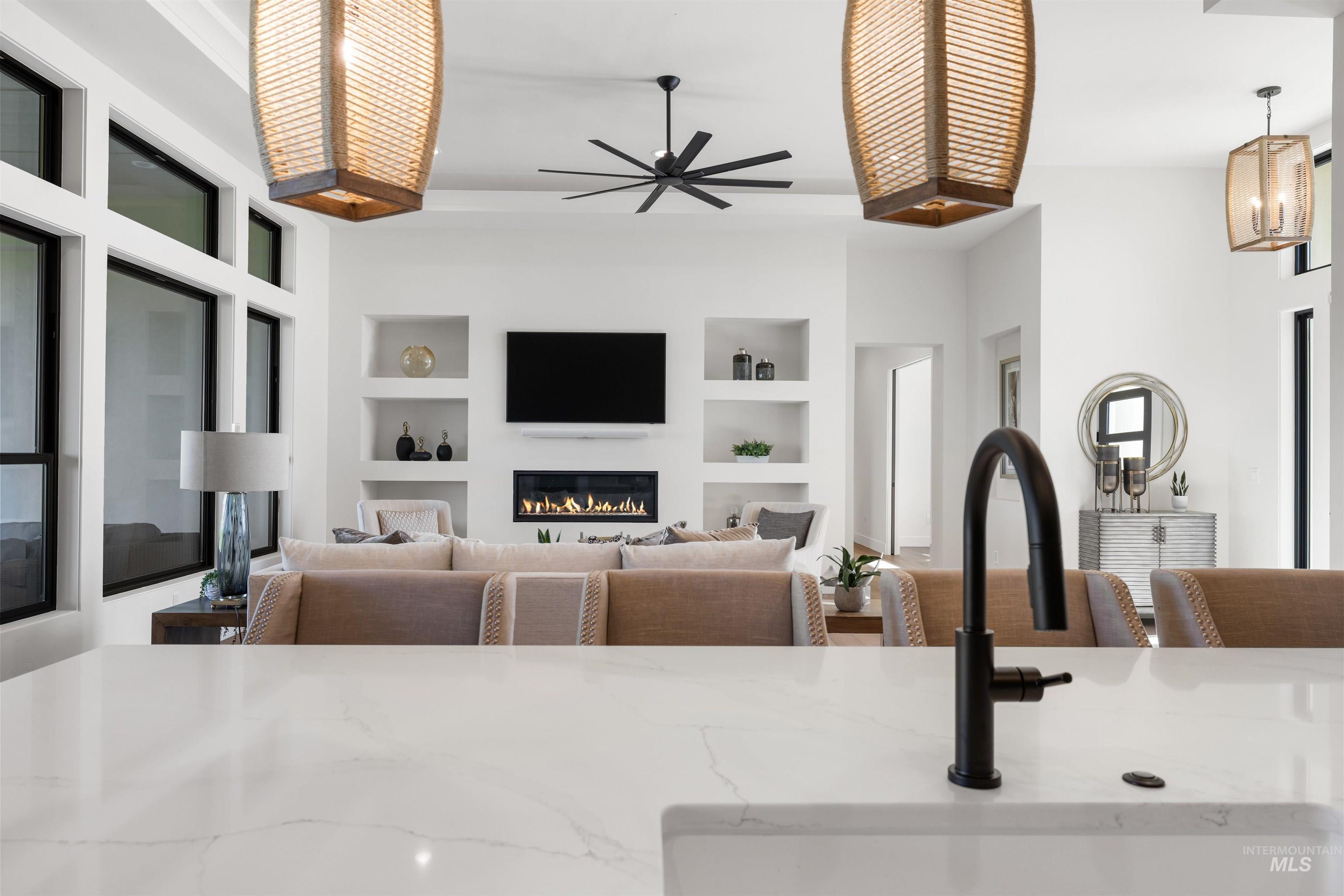 Living room featuring built in features, a glass covered fireplace, and ceiling fan