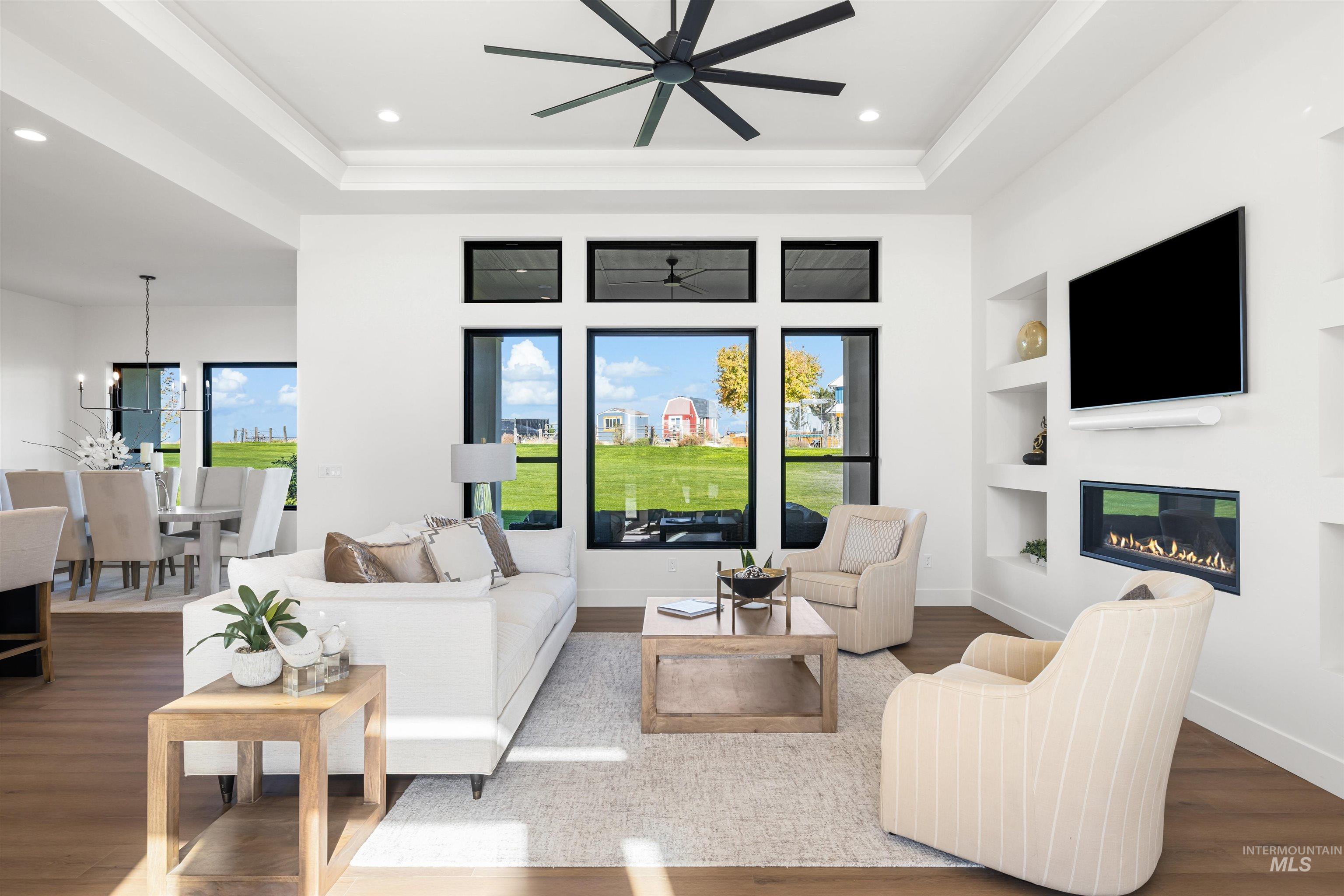 Living area with wood finished floors, recessed lighting, built in features, a glass covered fireplace, and a raised ceiling