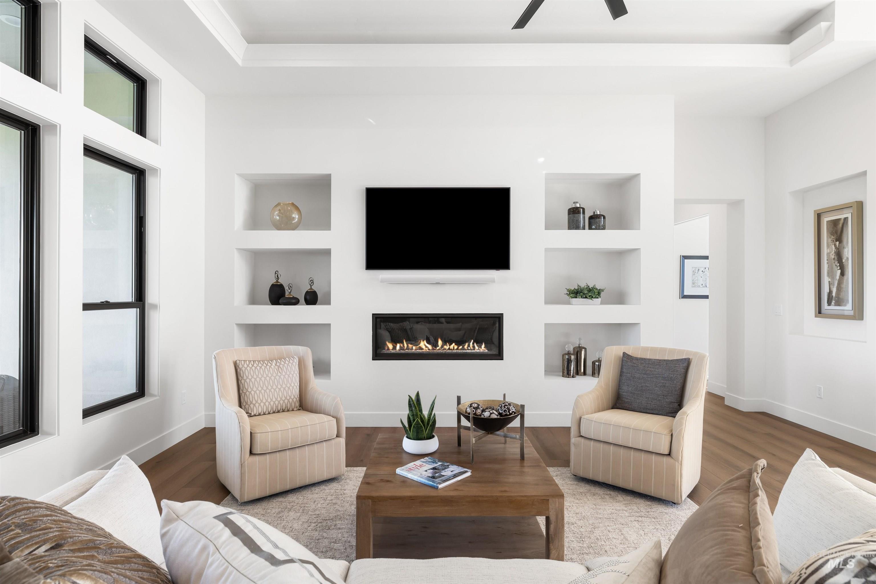 Living room with built in shelves, wood finished floors, a glass covered fireplace, and ceiling fan
