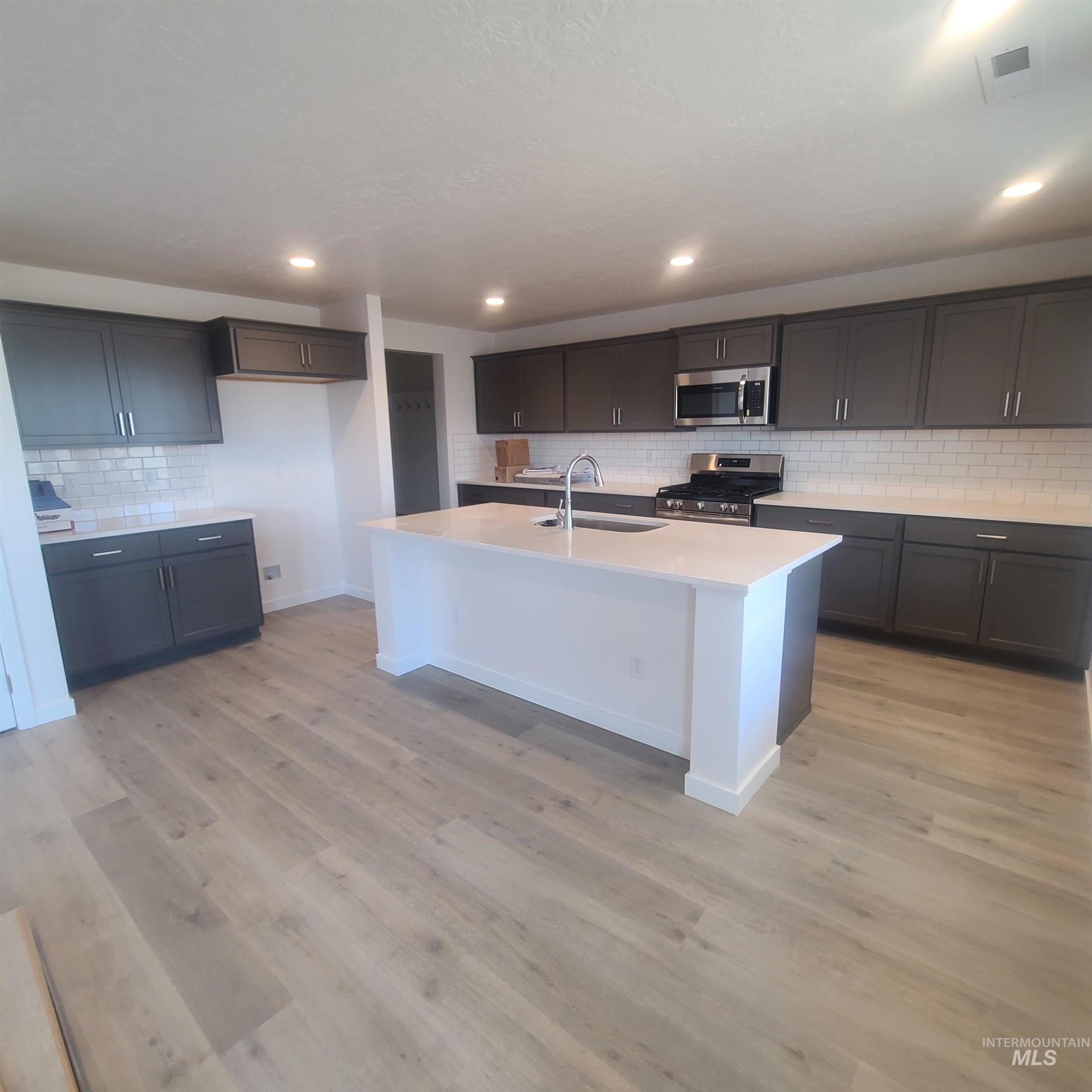 Kitchen with decorative backsplash, a center island with sink, stainless steel appliances, light wood-style floors, and recessed lighting