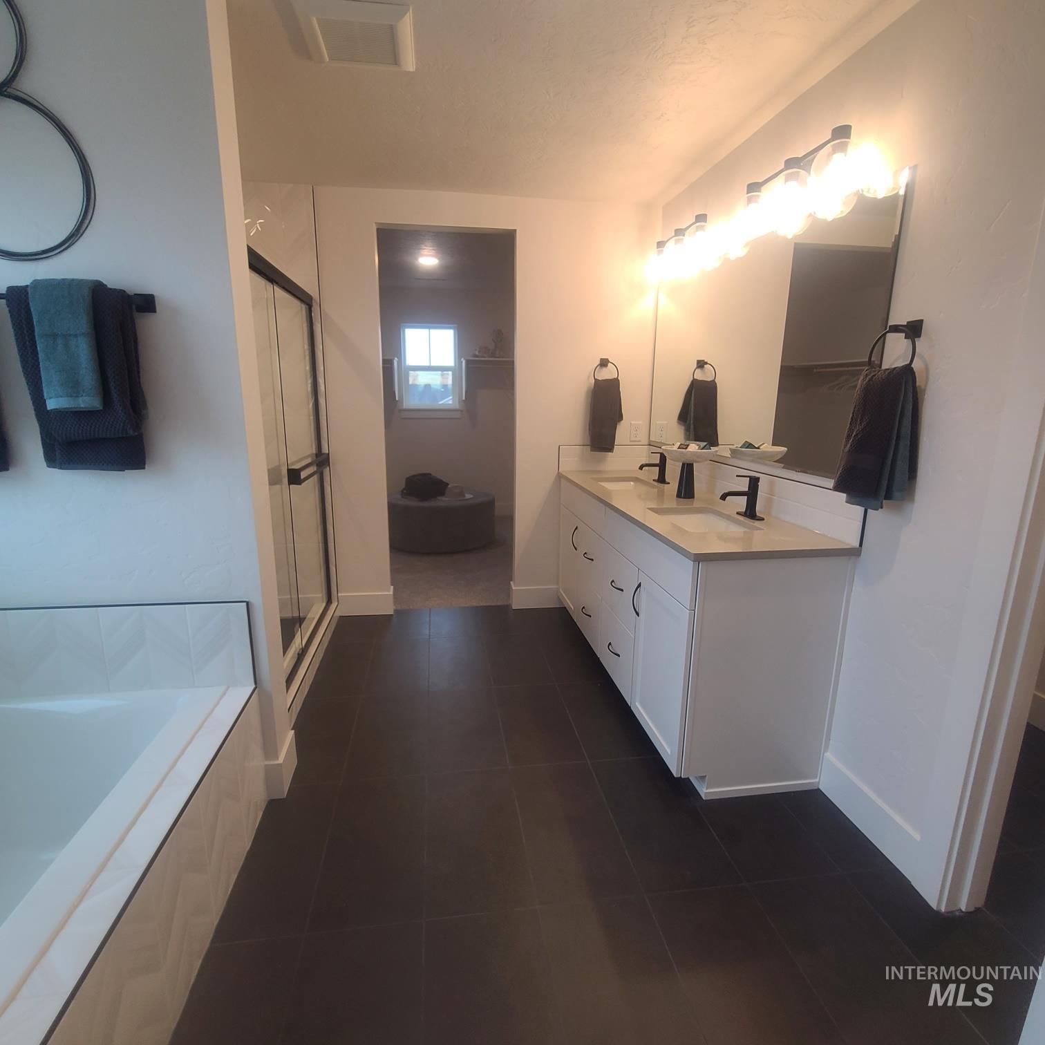 Full bathroom with a bath, double vanity, dark tile patterned floors, and a shower stall