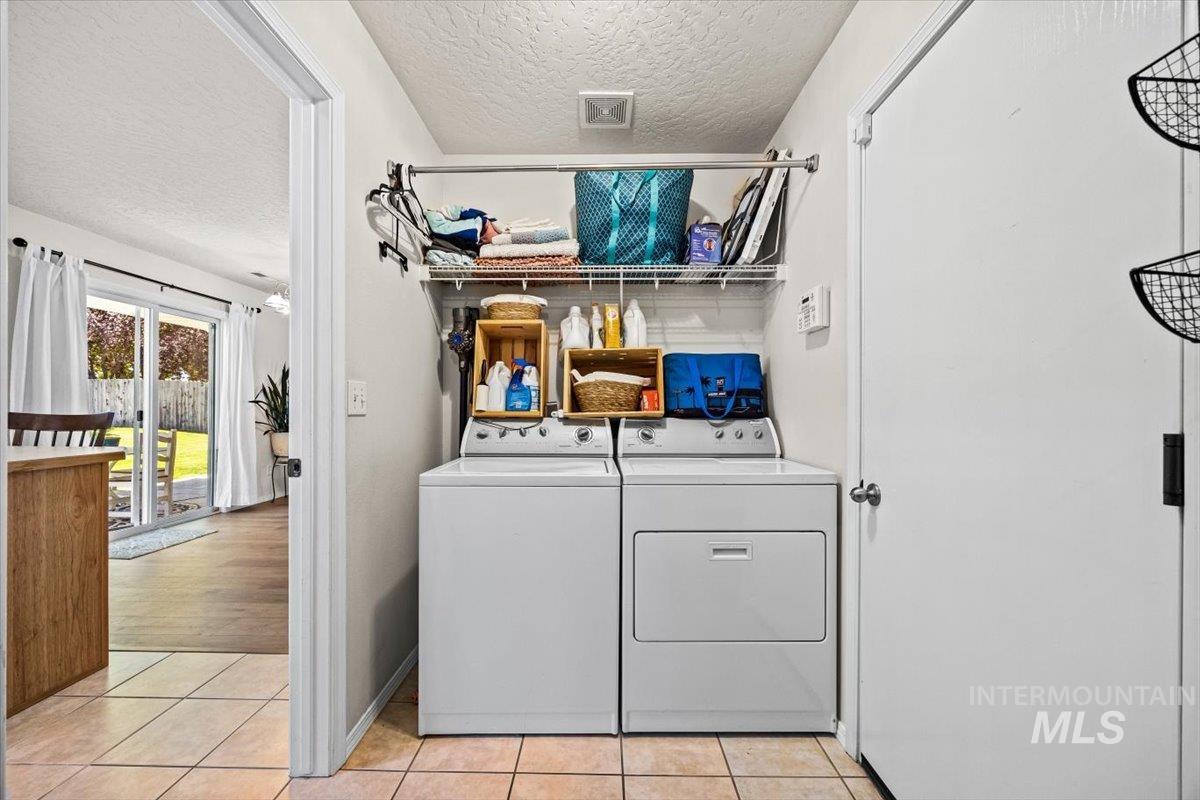 Laundry room with washer and dryer, a textured ceiling, and light tile patterned flooring