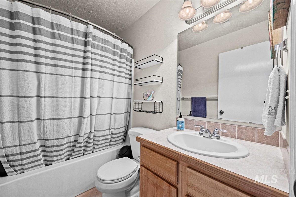 Bathroom featuring vanity, shower / bathtub combination with curtain, and a textured ceiling