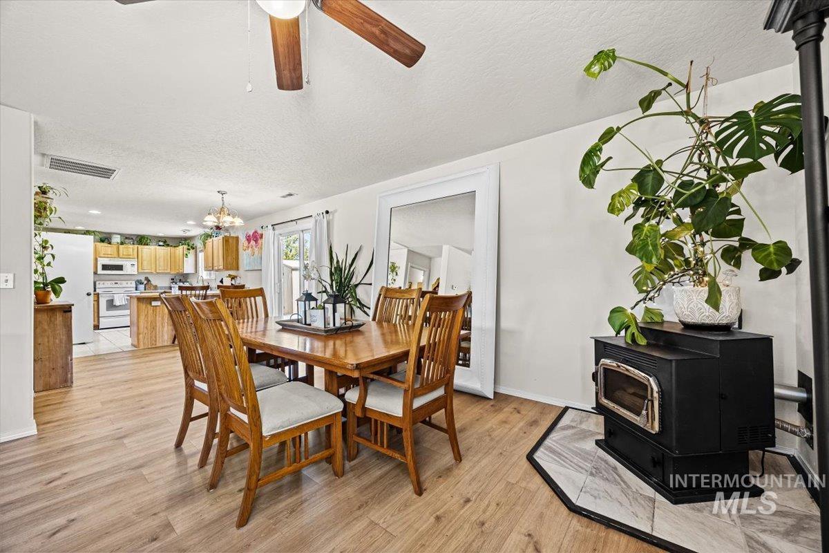 Dining room with a wood stove, a ceiling fan, a textured ceiling, light wood-style flooring, and a chandelier