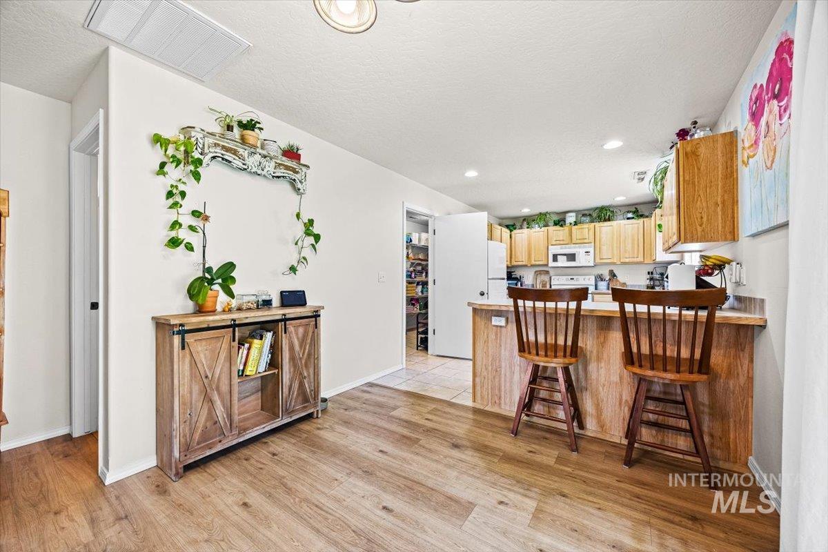 Kitchen with white appliances, light wood-style flooring, a kitchen breakfast bar, light countertops, and recessed lighting