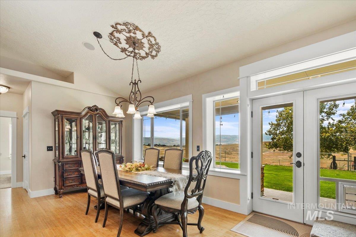 Dining space with light wood finished floors, a chandelier, vaulted ceiling, a textured ceiling, and french doors