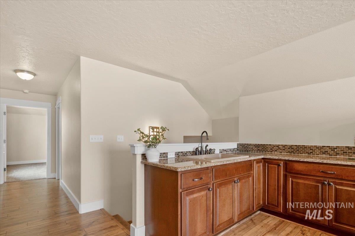 Kitchen featuring brown cabinets, light wood-style floors, a peninsula, a textured ceiling, and light stone counters