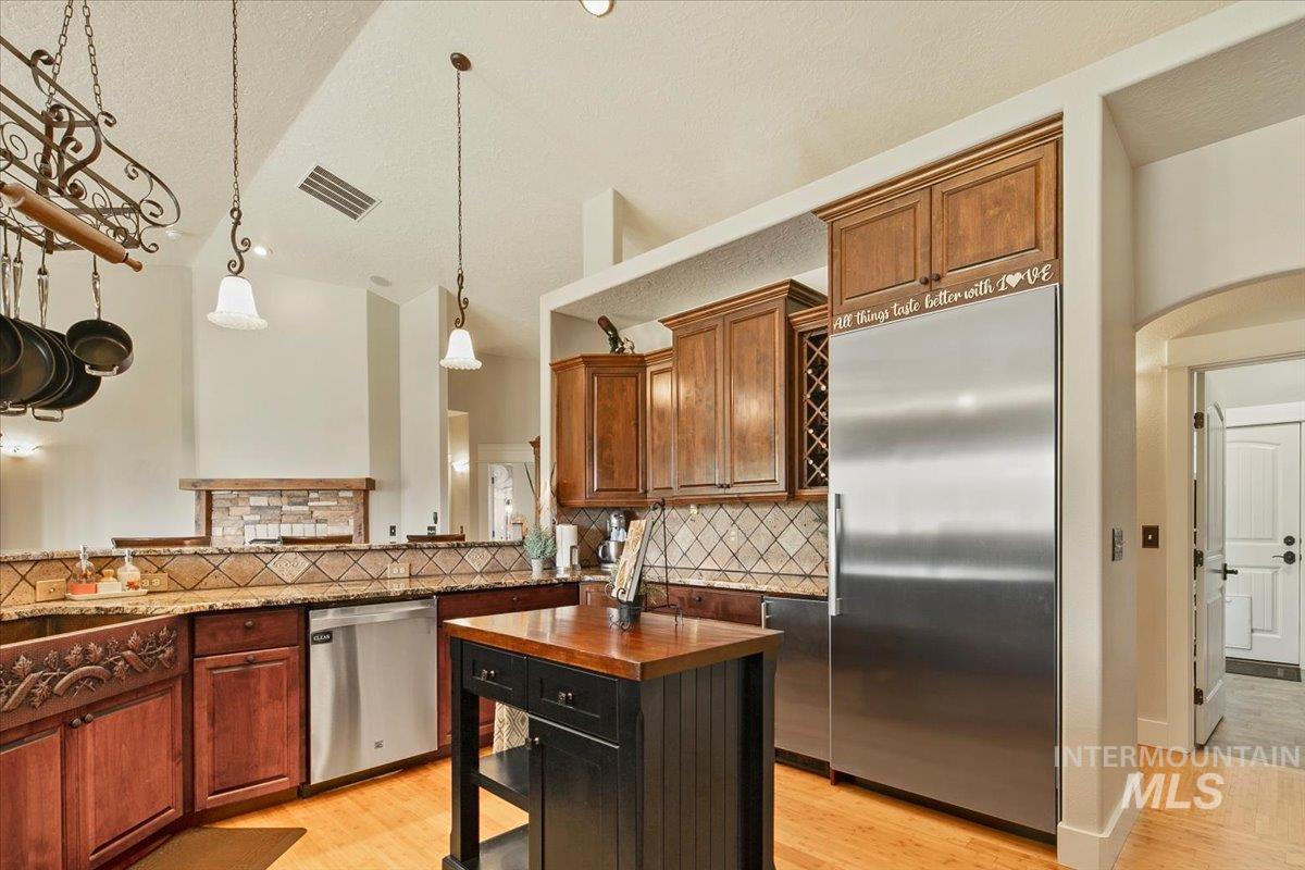 Kitchen featuring light wood-type flooring, appliances with stainless steel finishes, decorative light fixtures, dark stone counters, and arched walkways
