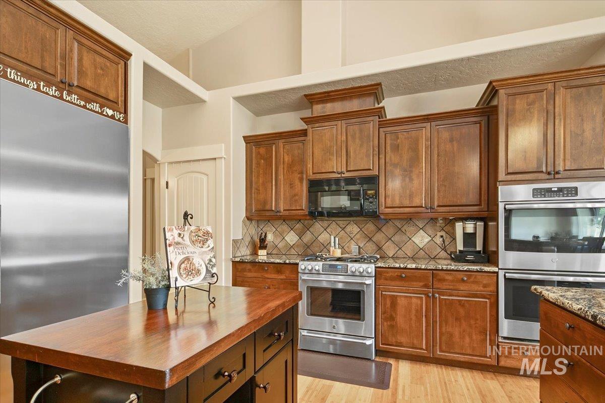 Kitchen featuring appliances with stainless steel finishes, brown cabinets, tasteful backsplash, light wood-style floors, and a textured ceiling