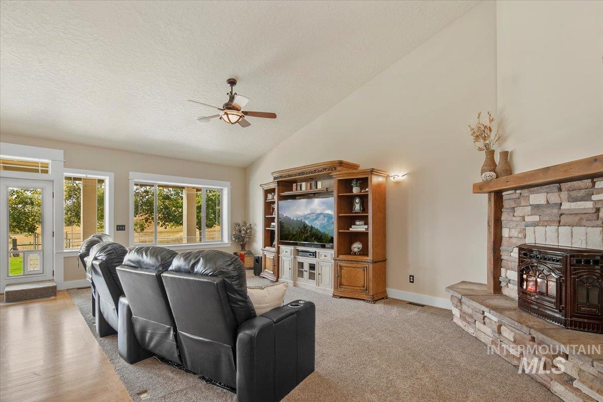 Living room with a textured ceiling, a ceiling fan, high vaulted ceiling, light colored carpet, and a wood stove