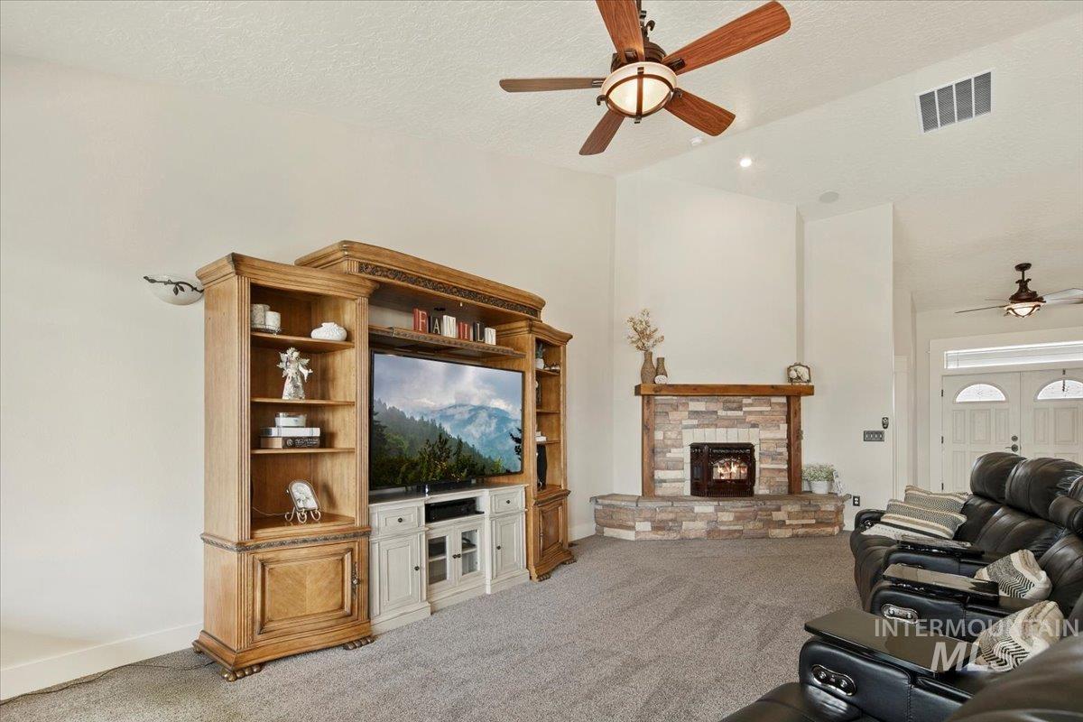 Living area featuring a ceiling fan, light colored carpet, a textured ceiling, and a stone fireplace