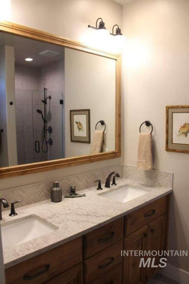 Bathroom featuring double vanity, a shower stall, and backsplash