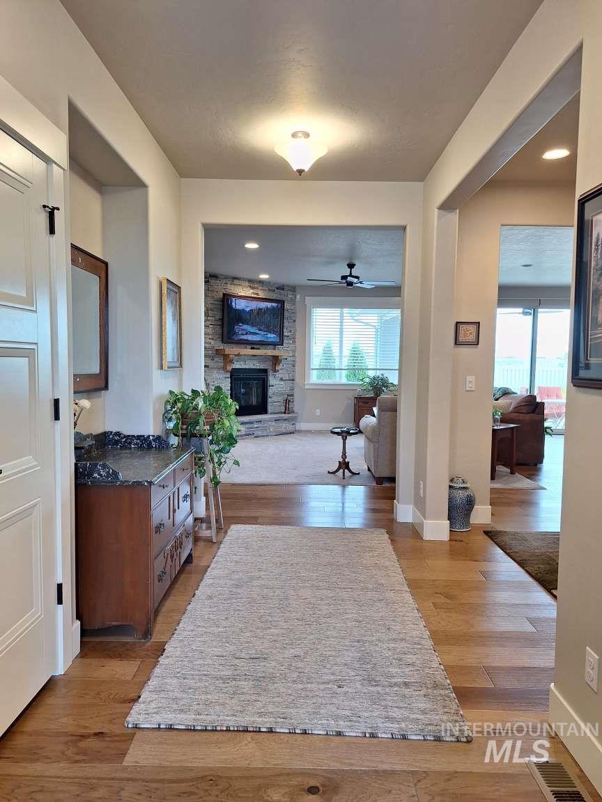 Living room featuring light wood-style flooring, a stone fireplace, and a ceiling fan