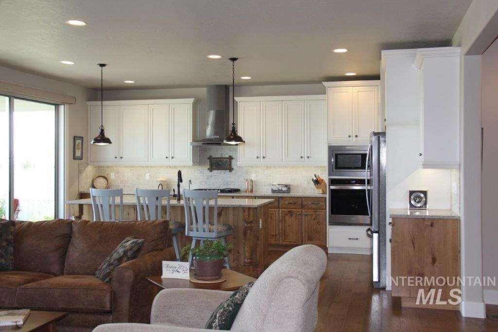 Kitchen featuring wall chimney exhaust hood, appliances with stainless steel finishes, open floor plan, decorative backsplash, and pendant lighting
