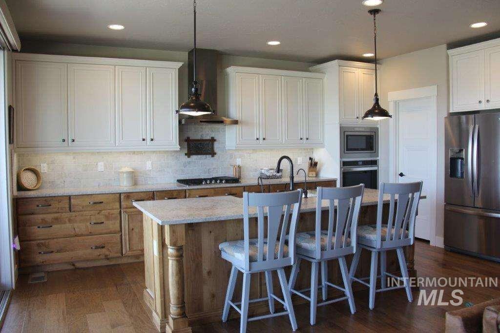 Kitchen with stainless steel appliances, pendant lighting, a center island with sink, backsplash, and wall chimney exhaust hood