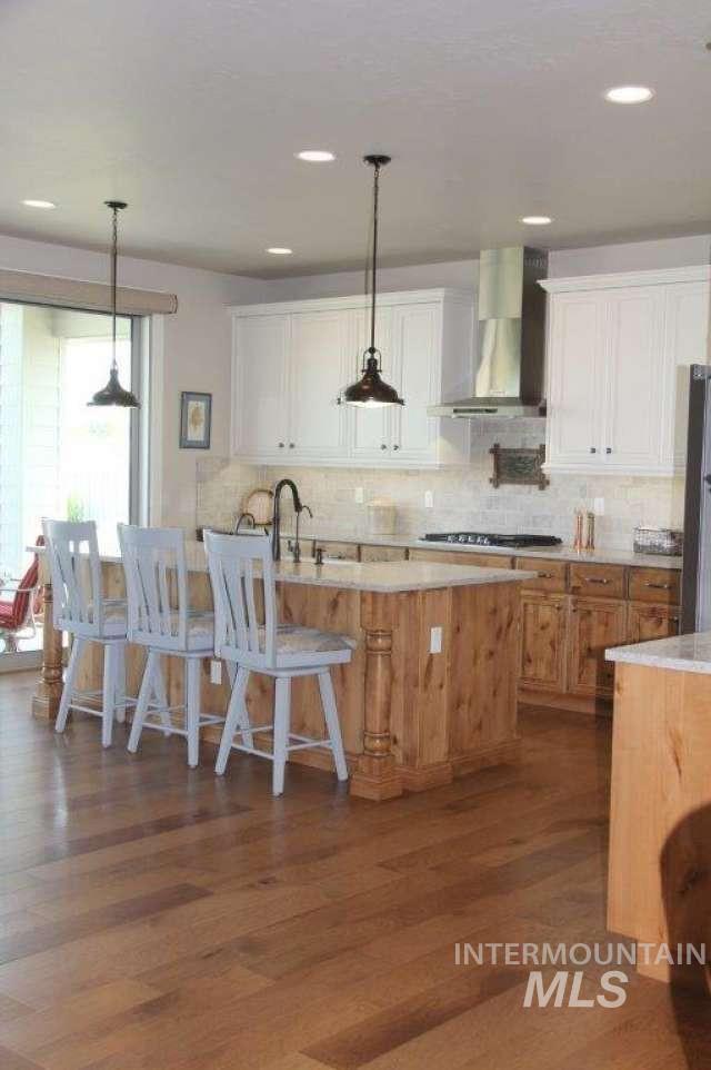 Kitchen with decorative light fixtures, tasteful backsplash, wall chimney exhaust hood, white cabinetry, and recessed lighting
