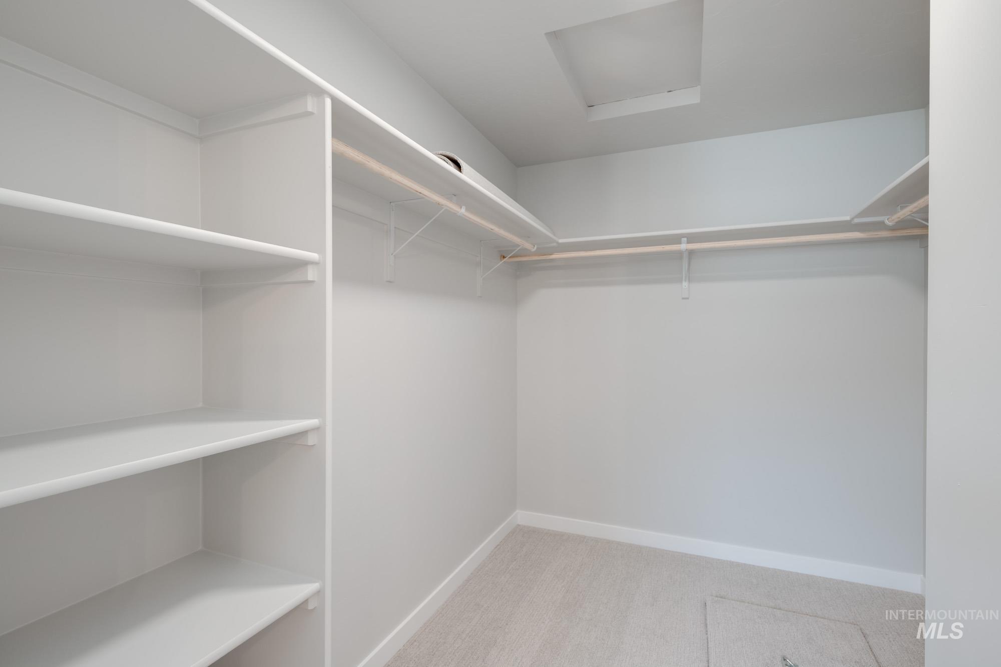 Walk in closet with light carpet and attic access