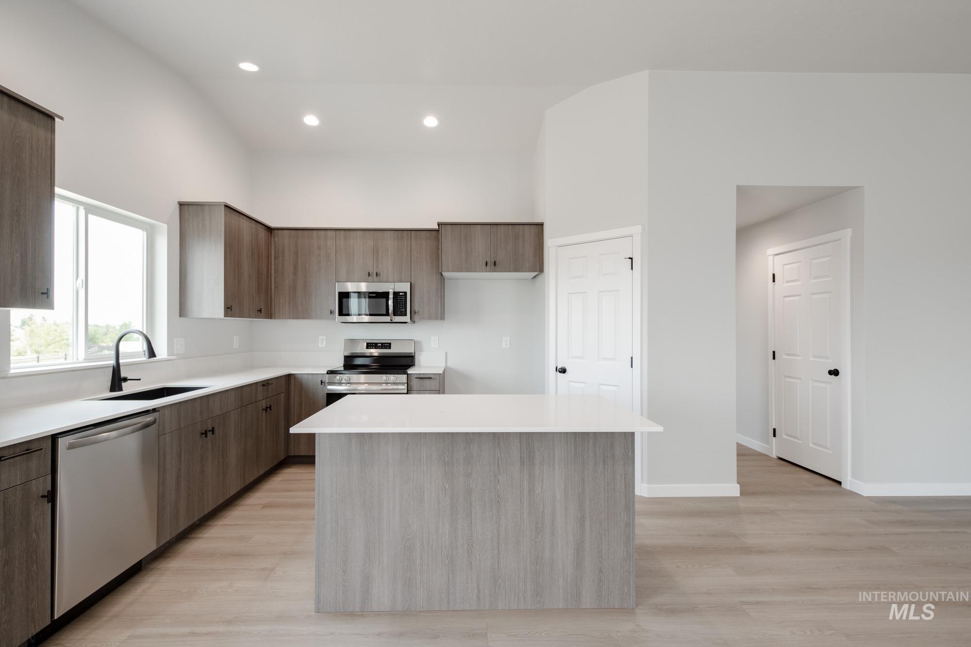 Kitchen featuring appliances with stainless steel finishes, modern cabinets, light countertops, light wood-style flooring, and a center island