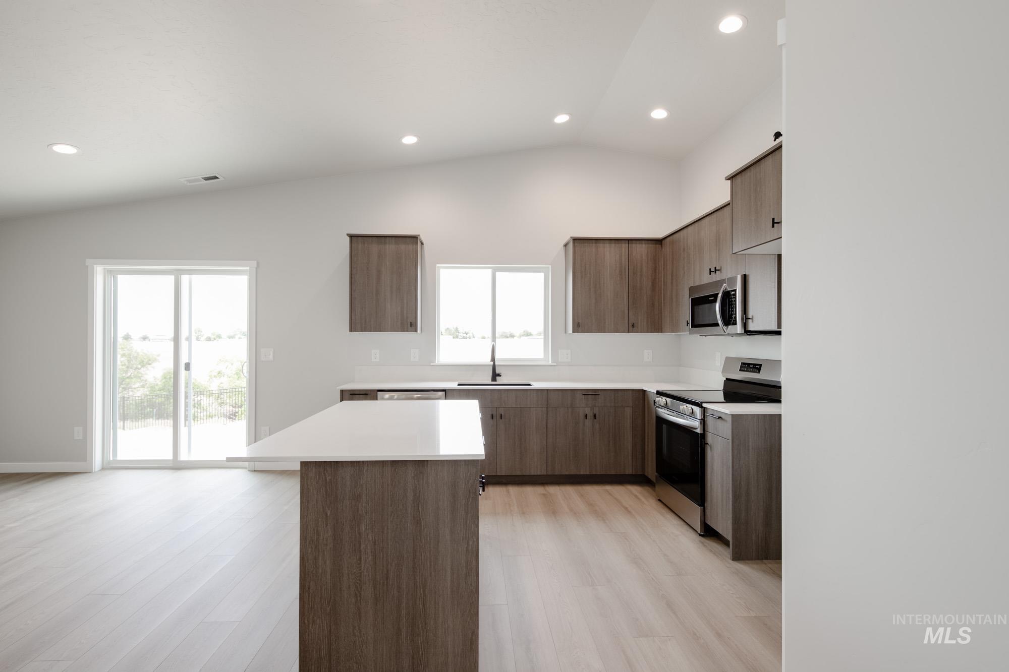 Kitchen with stainless steel appliances, light wood-style flooring, vaulted ceiling, a center island, and healthy amount of natural light