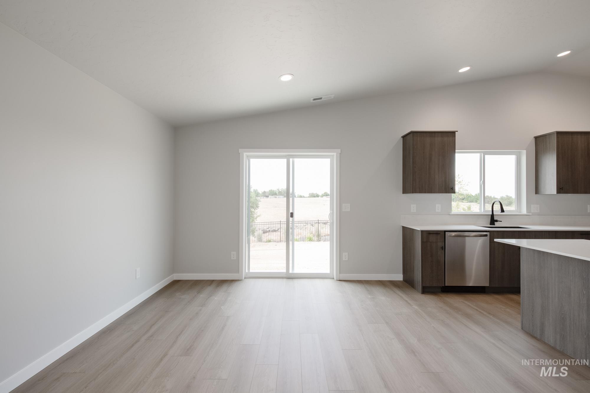 Kitchen featuring stainless steel dishwasher, vaulted ceiling, light wood-style flooring, light countertops, and plenty of natural light