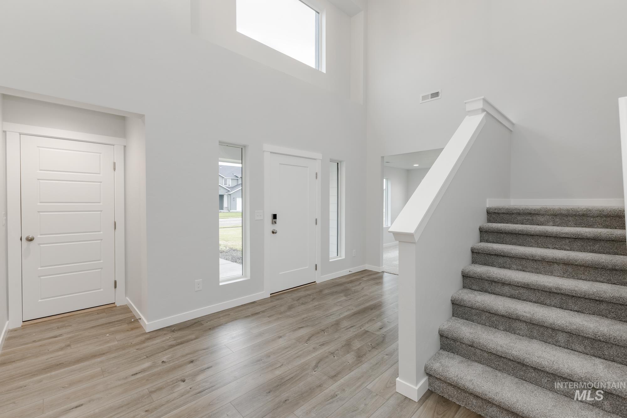 Foyer with healthy amount of natural light, light wood finished floors, stairway, and a high ceiling