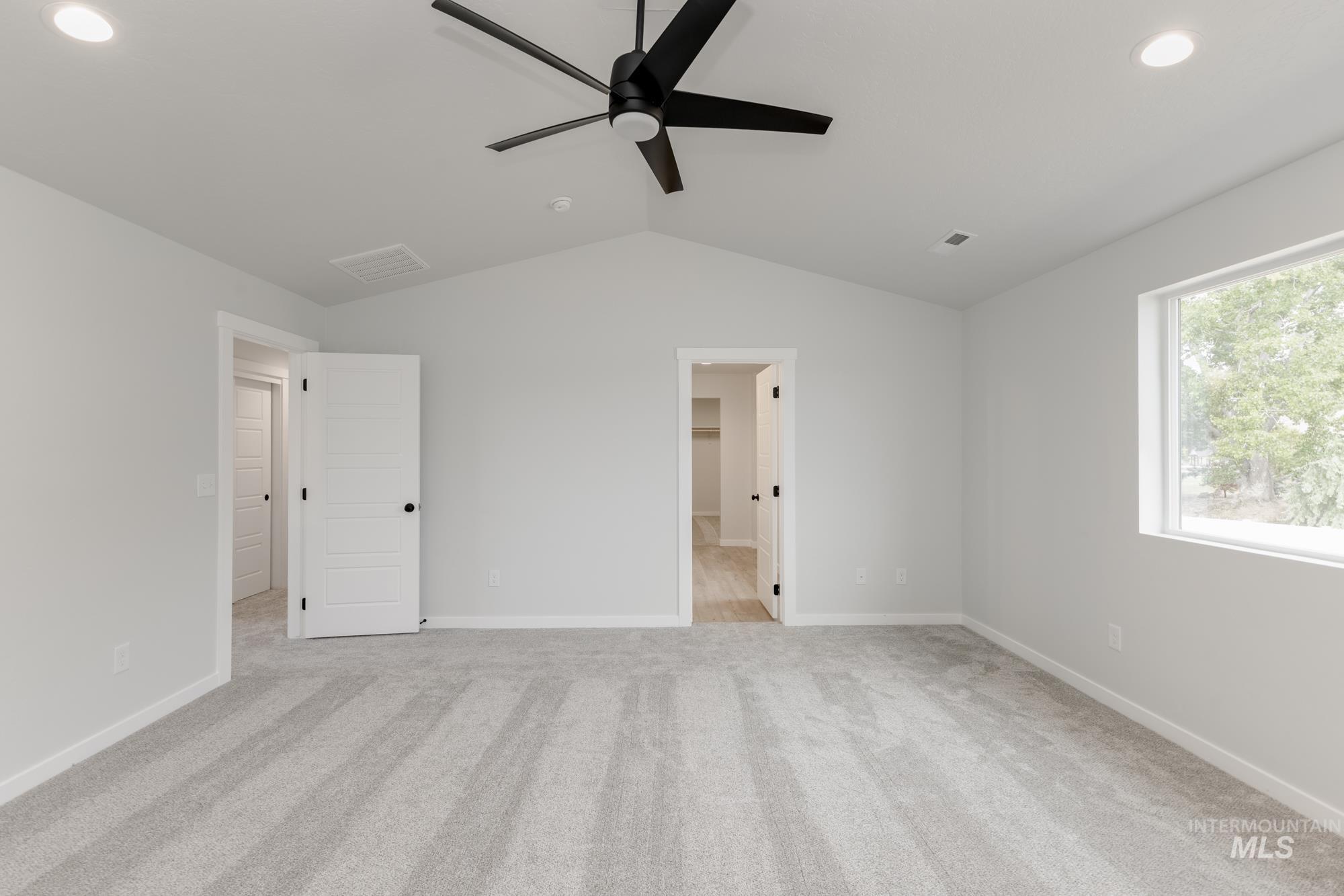 Unfurnished bedroom with lofted ceiling, light colored carpet, recessed lighting, a walk in closet, and a ceiling fan
