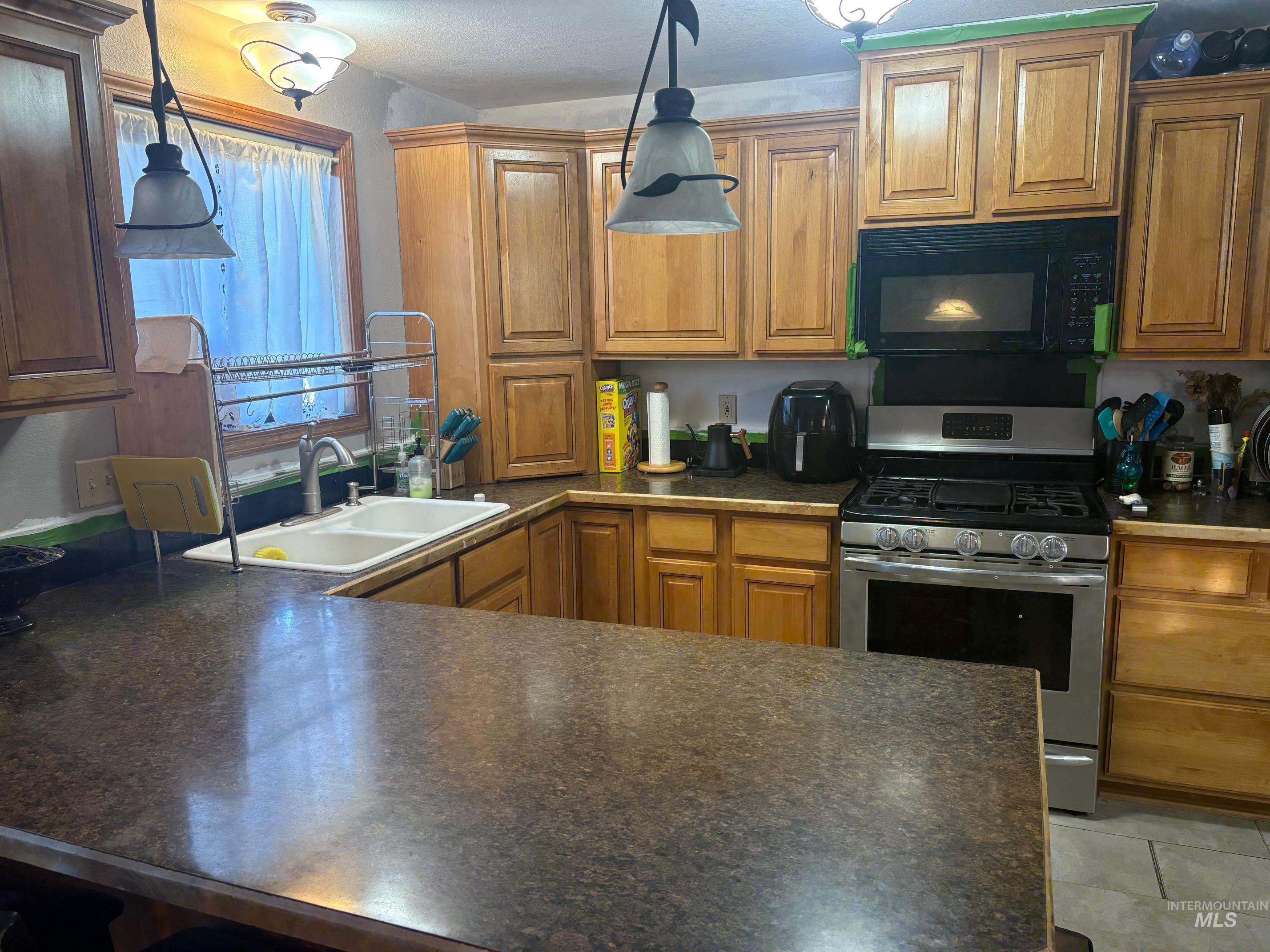 Kitchen with dark countertops, stainless steel range with gas stovetop, brown cabinets, and black microwave