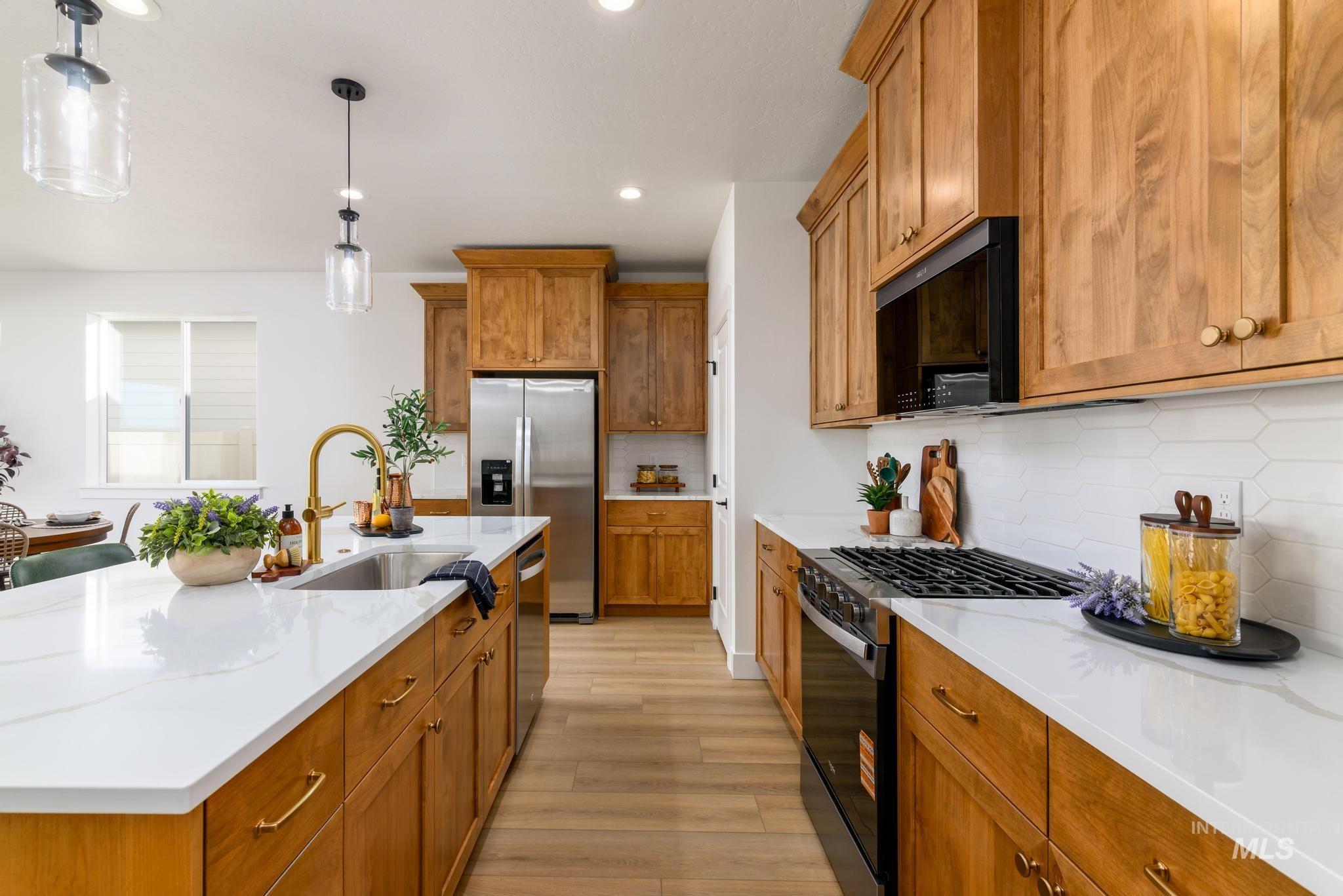 Kitchen with brown cabinets, black appliances, hanging light fixtures, tasteful backsplash, and light stone countertops