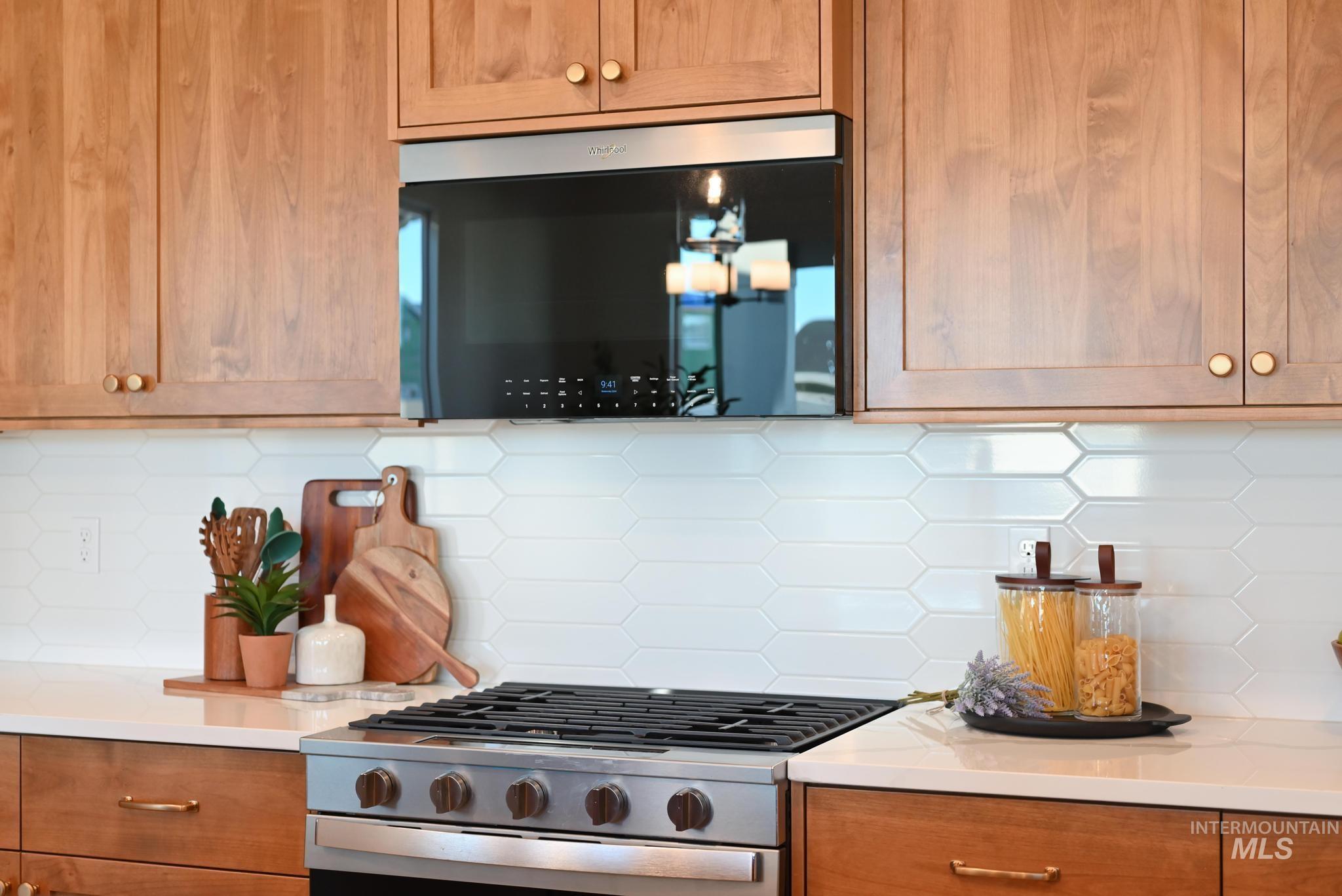 Kitchen with decorative backsplash, gas stove, brown cabinets, and light stone countertops