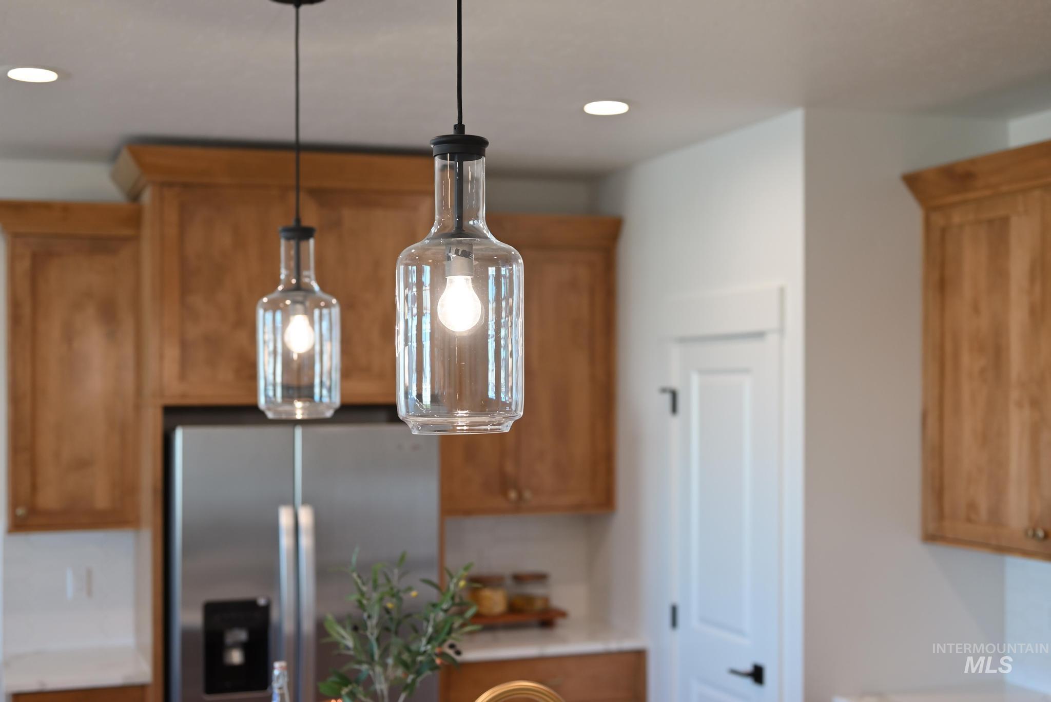 Kitchen view of stainless steel refrigerator with ice dispenser, brown cabinets, hanging light fixtures, light countertops, and recessed lighting