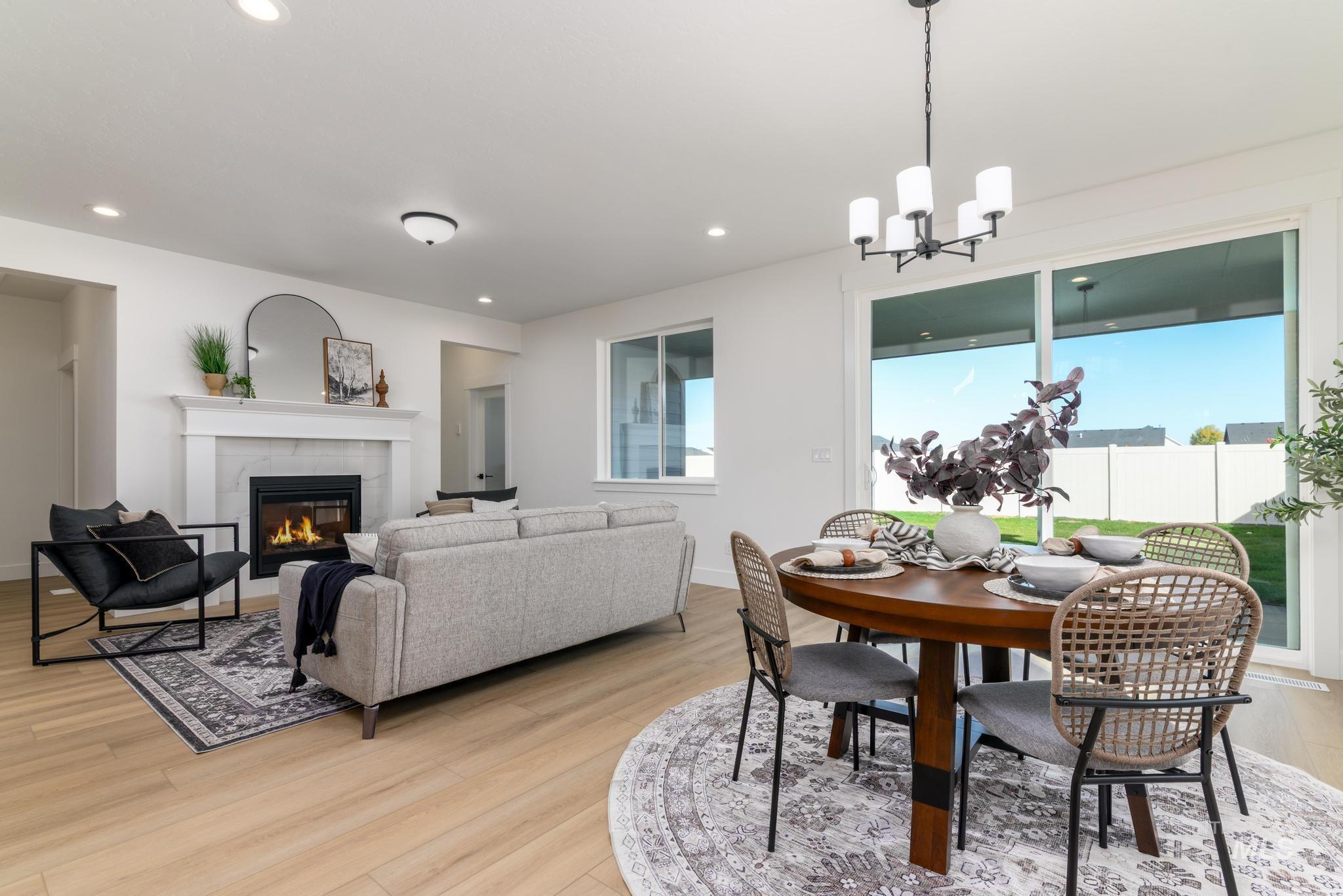 Dining room featuring healthy amount of natural light, a tiled fireplace, light wood finished floors, recessed lighting, and a chandelier