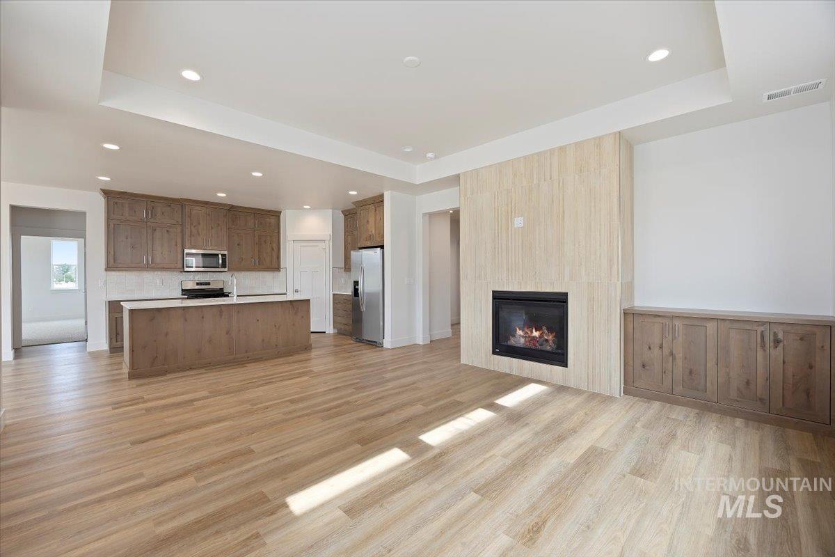 Unfurnished living room featuring a raised ceiling, light wood-style flooring, a fireplace, and recessed lighting