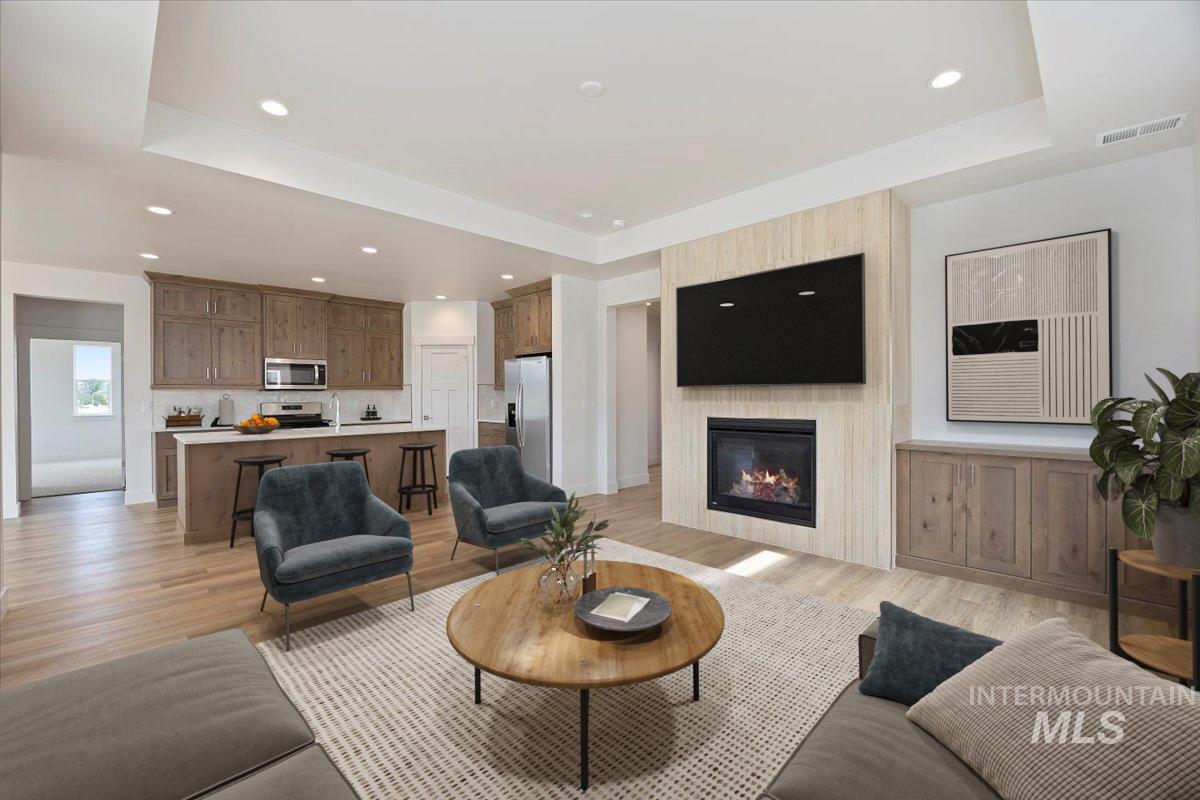 Living room featuring a raised ceiling, a large fireplace, light wood finished floors, and recessed lighting