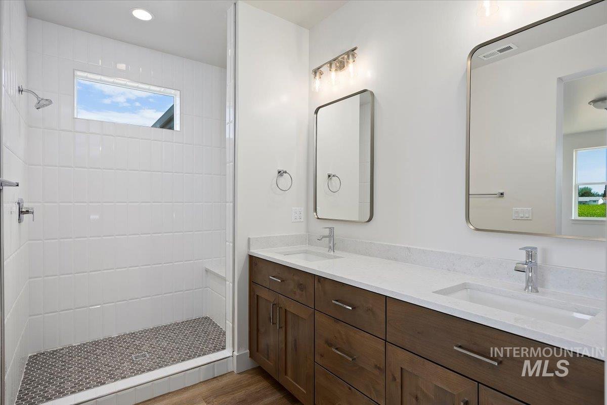 Bathroom with a tile shower, double vanity, plenty of natural light, and recessed lighting