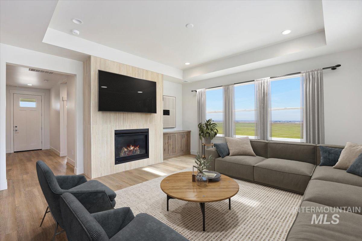 Living room featuring light wood finished floors, a tray ceiling, healthy amount of natural light, and recessed lighting