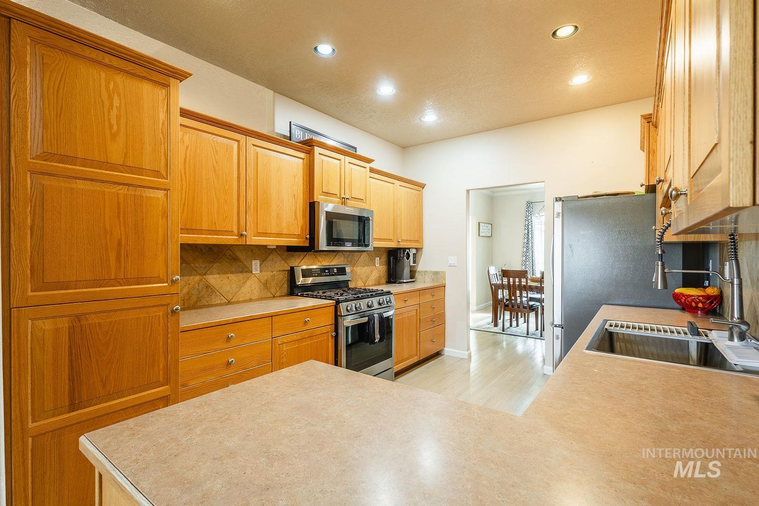Kitchen featuring appliances with stainless steel finishes, light countertops, recessed lighting, decorative backsplash, and light wood-style flooring