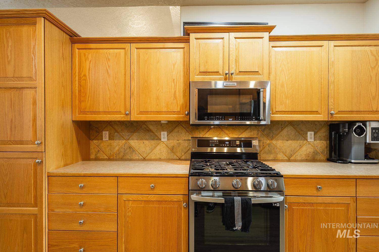 Kitchen featuring light countertops, appliances with stainless steel finishes, tasteful backsplash, and brown cabinetry