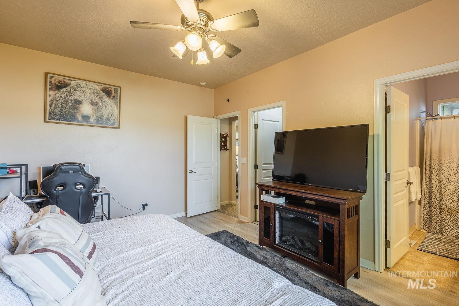Bedroom featuring light wood-style flooring, ceiling fan, a textured ceiling, and connected bathroom