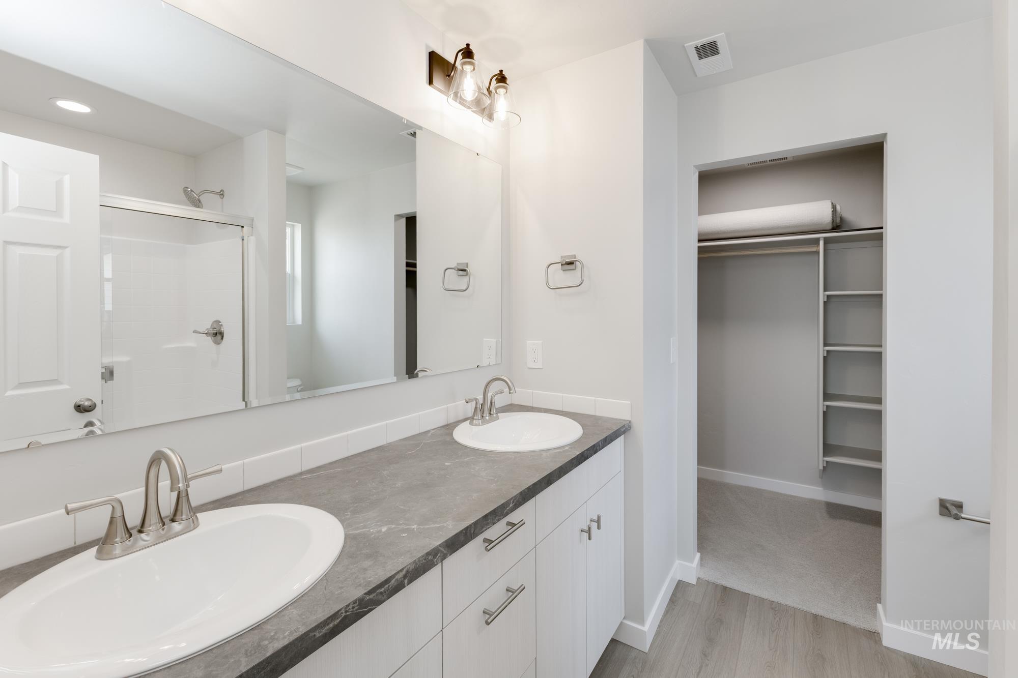 Bathroom featuring a shower with door, a walk in closet, double vanity, and wood finished floors