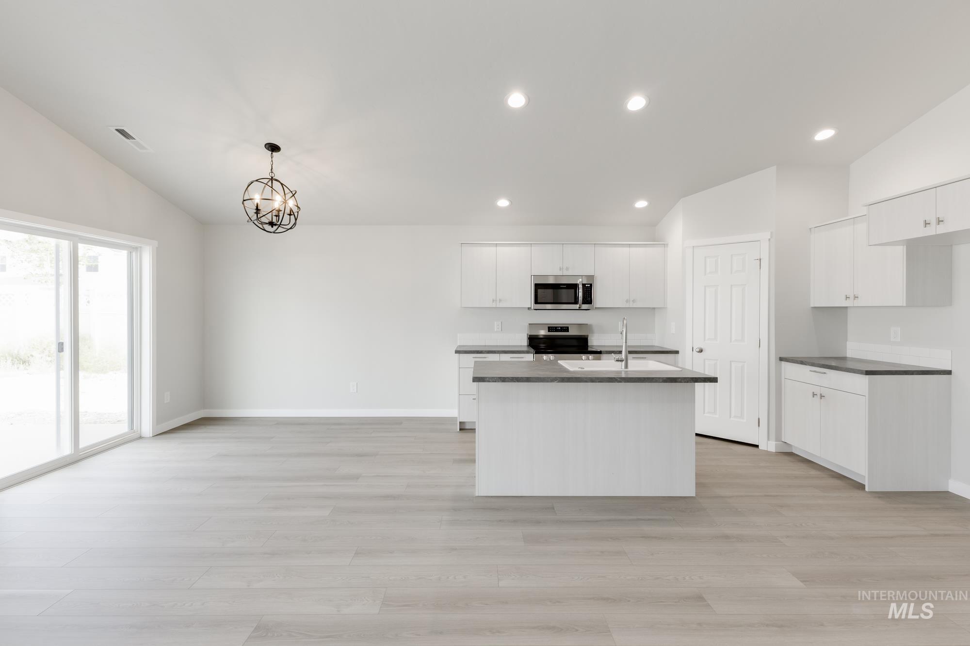 Kitchen with appliances with stainless steel finishes, vaulted ceiling, dark countertops, a chandelier, and recessed lighting