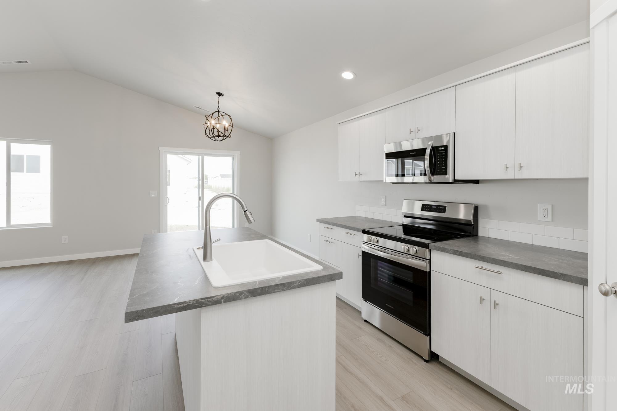 Kitchen featuring stainless steel appliances, light wood-style floors, vaulted ceiling, dark countertops, and a kitchen island with sink