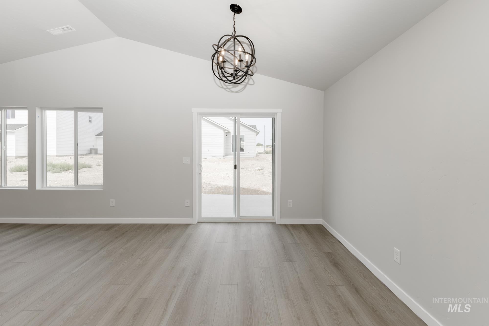 Unfurnished room featuring a chandelier, lofted ceiling, and light wood-style floors