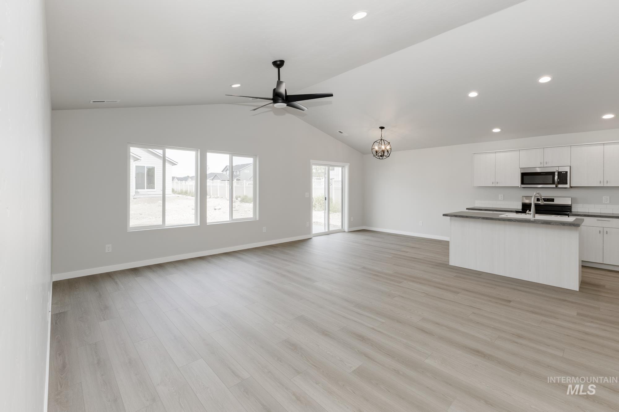 Unfurnished living room with a ceiling fan, recessed lighting, lofted ceiling, a chandelier, and light wood-style floors