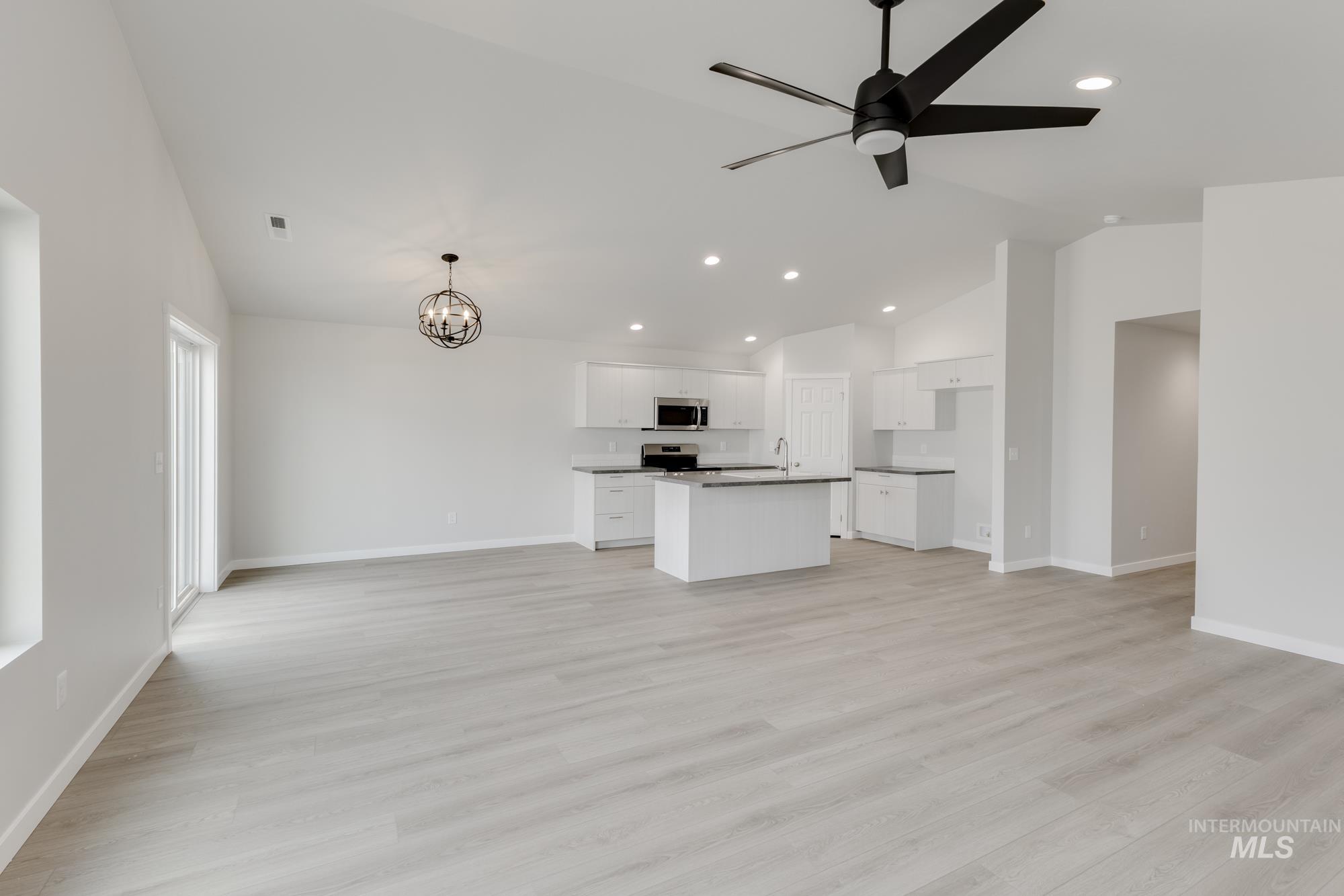 Unfurnished living room featuring vaulted ceiling, ceiling fan, a chandelier, recessed lighting, and light wood-style flooring