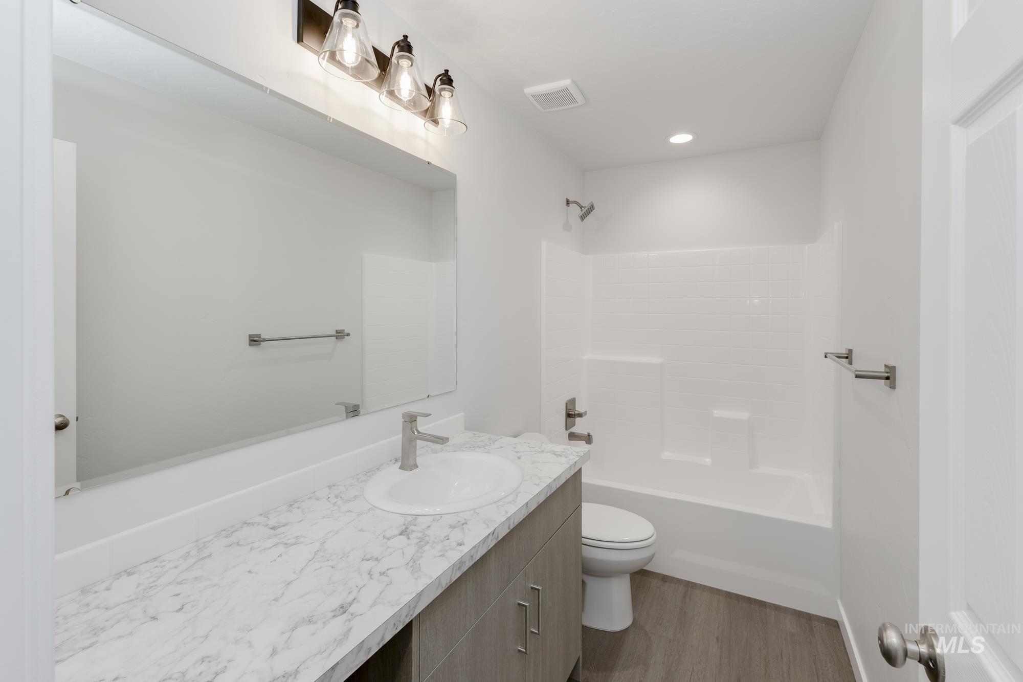 Bathroom featuring vanity, washtub / shower combination, wood finished floors, and recessed lighting