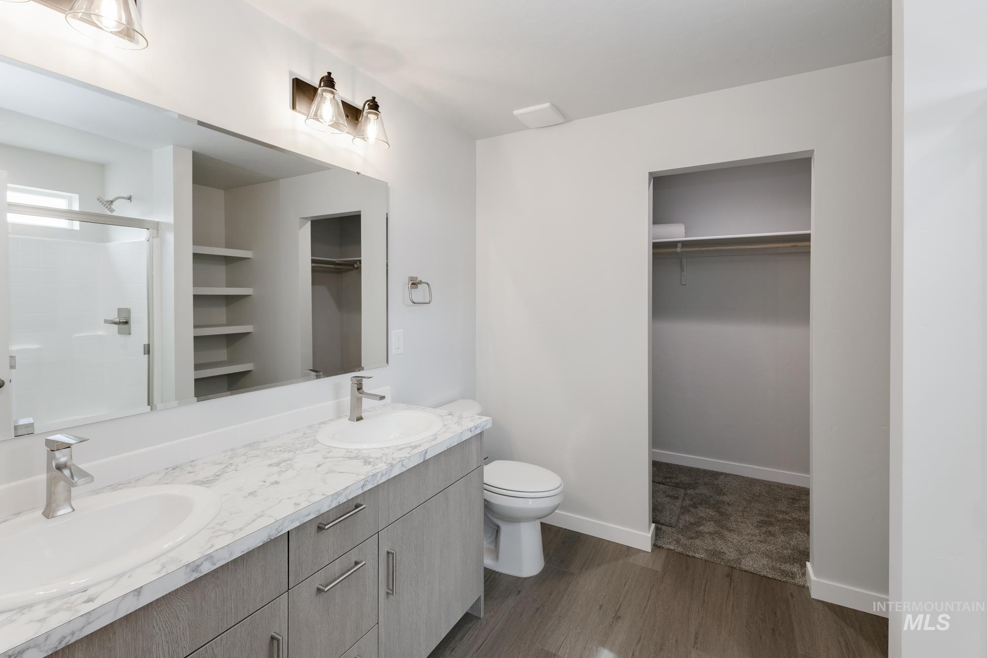 Bathroom featuring a spacious closet, wood finished floors, double vanity, and a shower with shower door