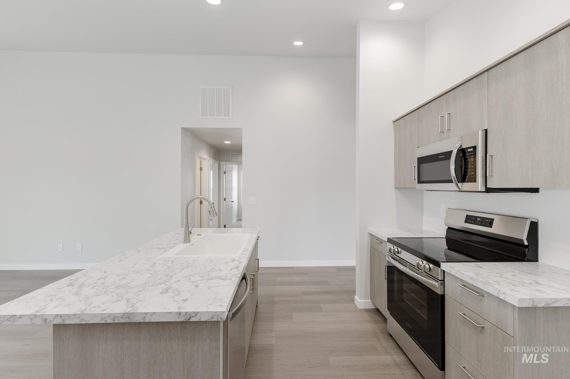Kitchen with stainless steel appliances, light brown cabinetry, modern cabinets, light wood finished floors, and light countertops