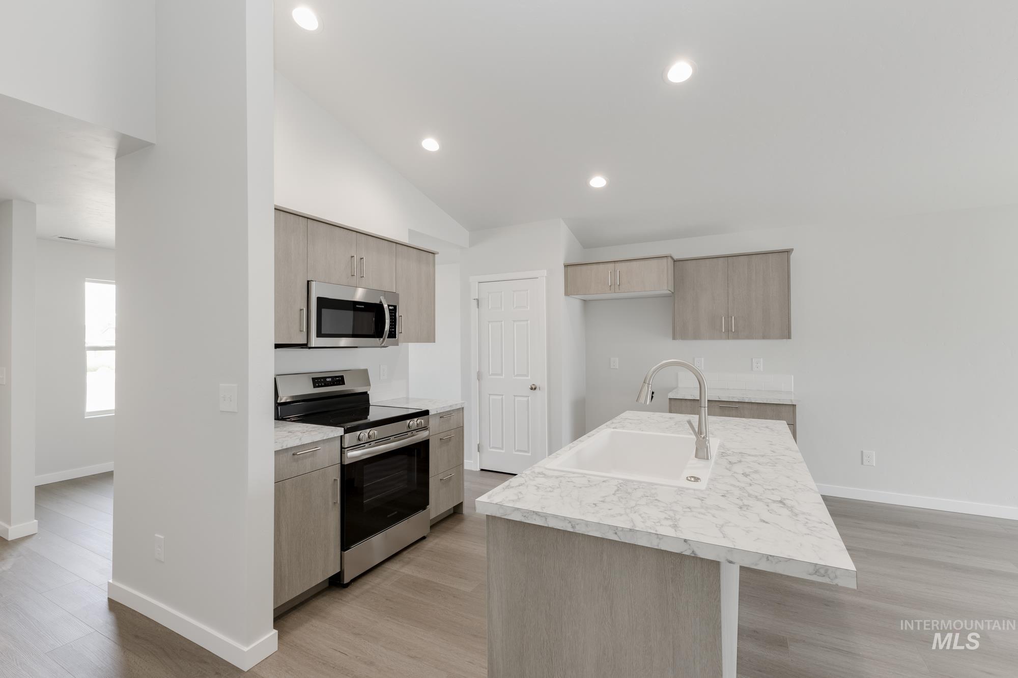 Kitchen featuring appliances with stainless steel finishes, light countertops, light wood finished floors, a kitchen island with sink, and vaulted ceiling